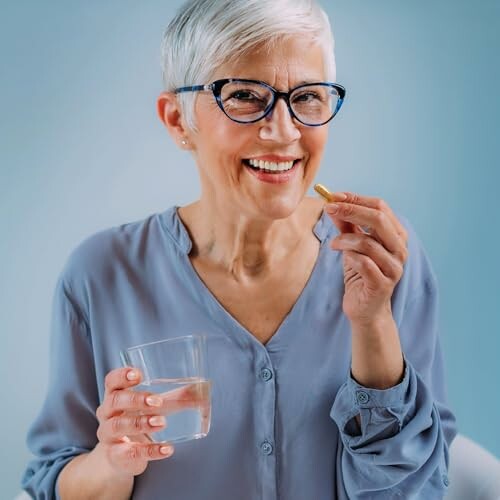 Ältere Frau mit Brille hält ein Glas Wasser und eine Pille.